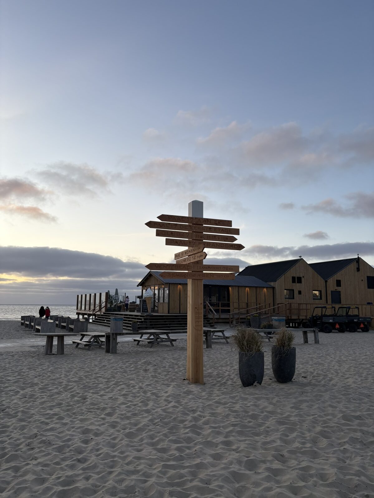 Strand op Texel met houten wegwijzer richting paalpaal-strandtenten bij zonsondergang.